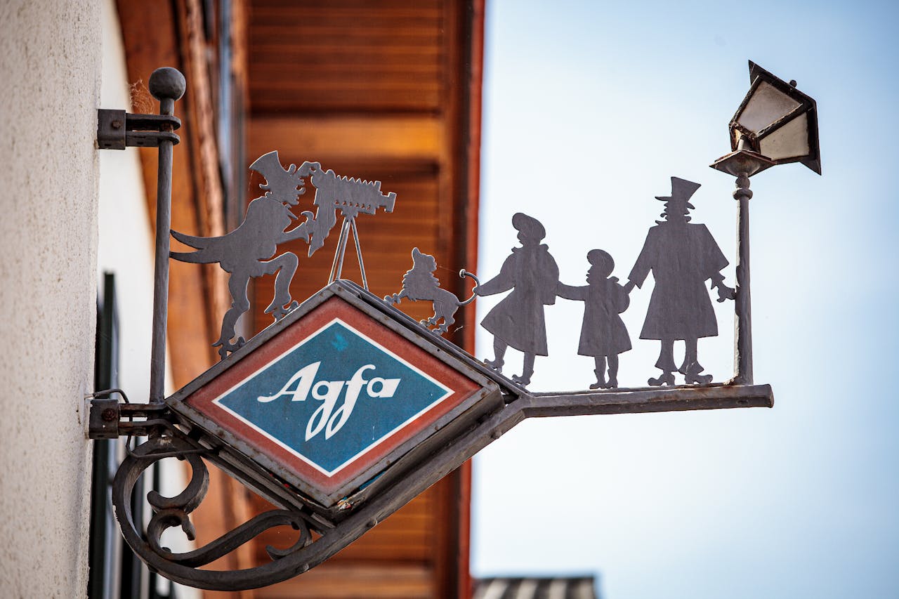 Vintage Agfa shop sign showcasing silhouette figures against a clear sky, reminiscent of old European charm.